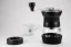 Manual Hario Skerton Pro black coffee grinder on a white table, with a white porcelain cup in the background.
