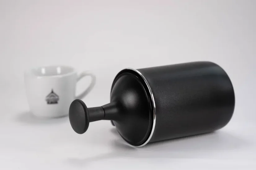 Milk frother from the top in a black finish by Bialetti Tuttocrema with a capacity of 330ml on a white background, accompanied by a cup with a coffee logo.