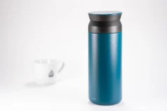 Botella térmica de acero inoxidable azul de 500 ml sobre fondo blanco con una taza de café.