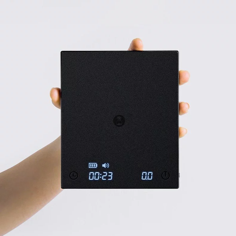 Hand holding a Black Mirror barista digital scale, top view