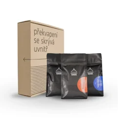 Braune Pappschachtel mit der Aufschrift "Überraschung verbirgt sich im Inneren" auf weißem Hintergrund mit drei Paketen Kaffeebohnen in schwarzer Verpackung.