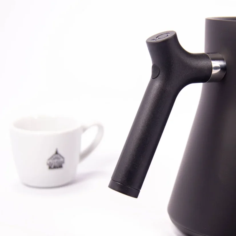 Bouilloire électrique noire sur fond blanc avec une tasse de café, détail sur la poignée de la bouilloire