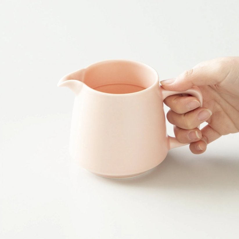 taza de porcelana para café de filtro en color rosa, agarrada entre las manos.