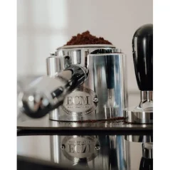 Portafilter in a tamping station with ground coffee in the basket.