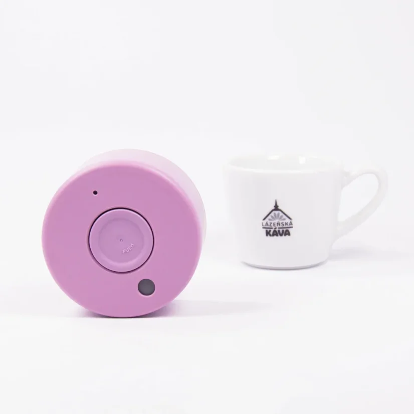 Detail of the lid of a pink thermal bottle from above, with a white background and a cup of coffee.