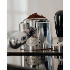 Portafilter in a tamping station with ground coffee in a cup.