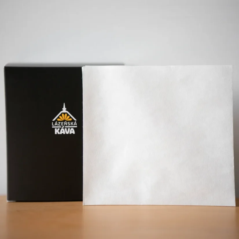 Weiße Papierfilter, schwarze Schachtel mit Logo auf weißem Hintergrund auf einem Holztisch