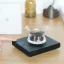 Čierna váha so stopkami ležiaca na drevenom stole so sklenenou nádobou s mletou kávou