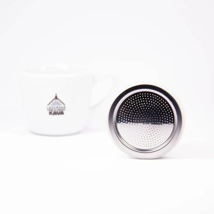 Filtro argentato per caffettiera moka Bialetti appoggiato su un bordo su uno sfondo bianco con una tazza di caffè