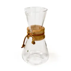 Chemex en verre avec une tête allongée, poignée en bois et lanière en cuir. Chemex en verre avec une tête allongée, poignée en bois et lanière en cuir.