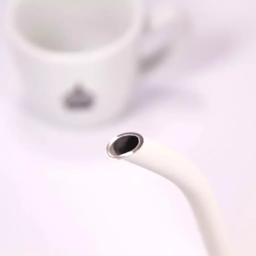 White electric kettle, detail on the spout with a coffee cup in the background.