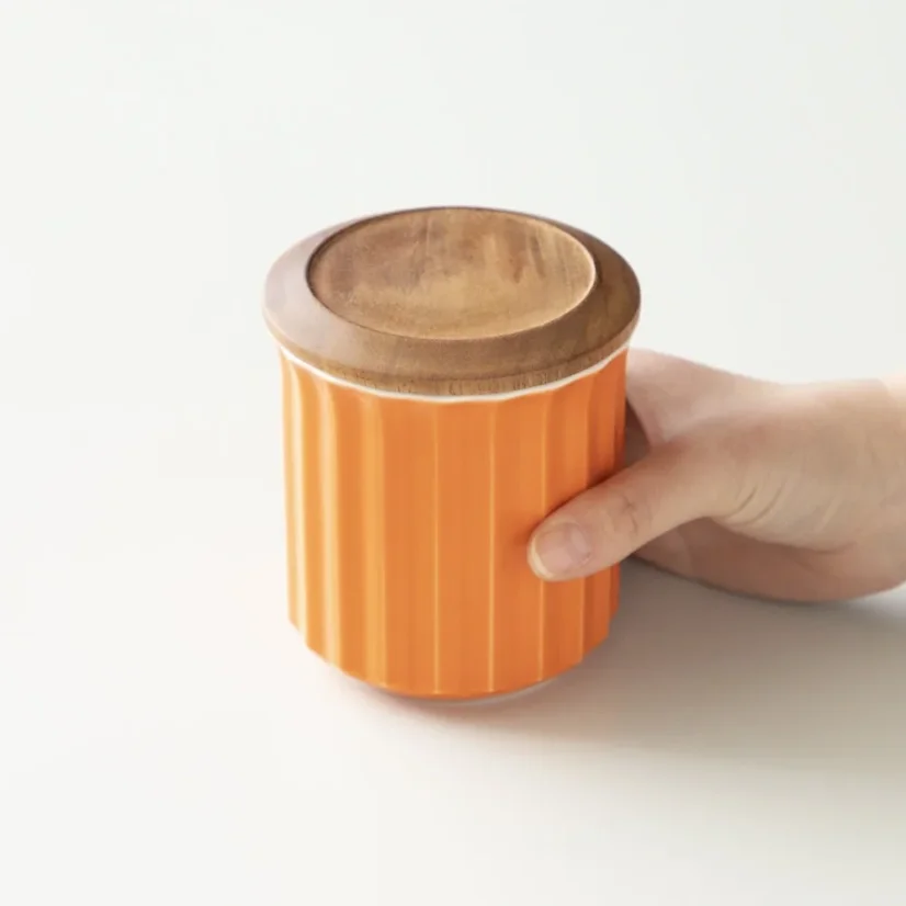 Récipient en porcelaine avec un couvercle en bois dans la main.