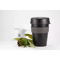 Gobelet thermique noir en plastique avec poignée grise sur une table blanche avec une plante, tasse blanche sur fond blanc. Gobelet thermique noir en plastique avec poignée grise sur une table blanche avec une plante, tasse blanche sur fond blanc.