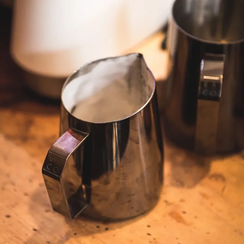 Stainless steel pitcher from Barista and Co Dial In Milk Pitcher 420ml in a dark finish with frothed milk