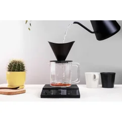 Balanza Felicita Parallel Plus durante el vertido de café filtrado con una jarra y un cactus.