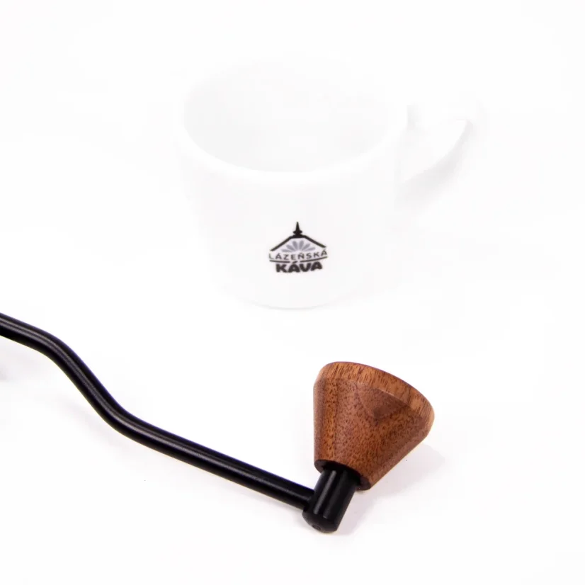 Detail of a handle with a wooden grip on a Timemore manual coffee grinder on a white background with a cup of coffee.