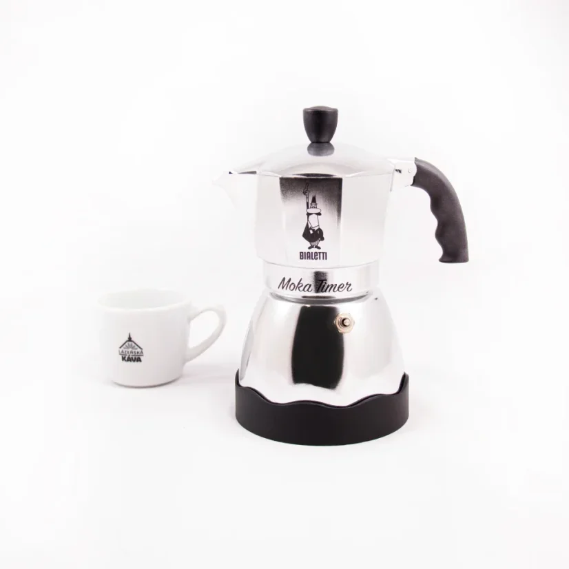 Side view of a silver Bialetti Moka Timer coffee maker with a cup featuring a coffee logo in the background.