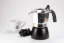 Silver Bialetti Brikka moka pot with a black water chamber, placed on a table with grape wine and a porcelain cup with a coffee logo.