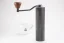 Kvalitný mlynček na kávu značky Timemore s pevným hliníkovým telom a dreveným držadlom na pozadí s naším šálkom na kávu.