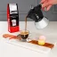 serving coffee from an aluminum Bialetti moka pot into a clear cup on a wooden board with a bag of coffee and small macarons