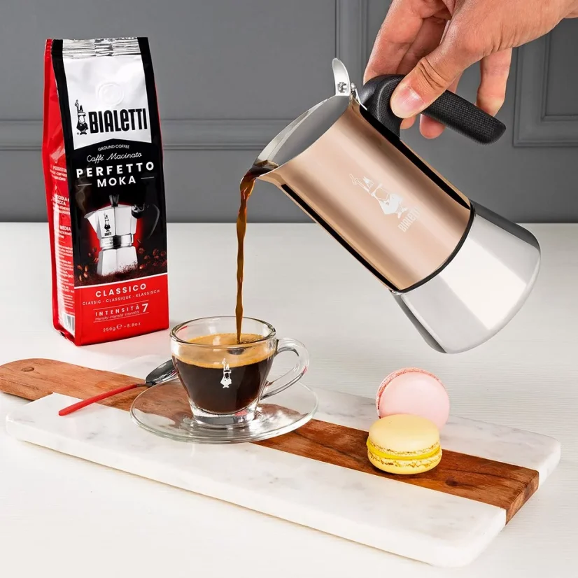 Serving coffee prepared in a Bialetti New Venus Copper pot into a clear cup, with a package of coffee suitable for this brewing method in the background.