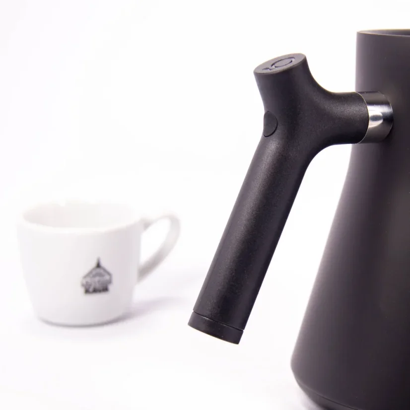 Black electric kettle on a white background with a cup of coffee, detail on the kettle's handle