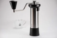 Manual coffee grinder by Kinu, model Simplicity, with a coffee cup in the background. Manual coffee grinder by Kinu, model Simplicity, with a coffee cup in the background.