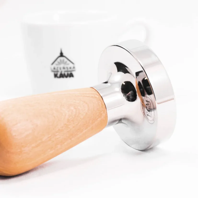 Detail of a tamper with an olive wood handle with coffee in the background.
