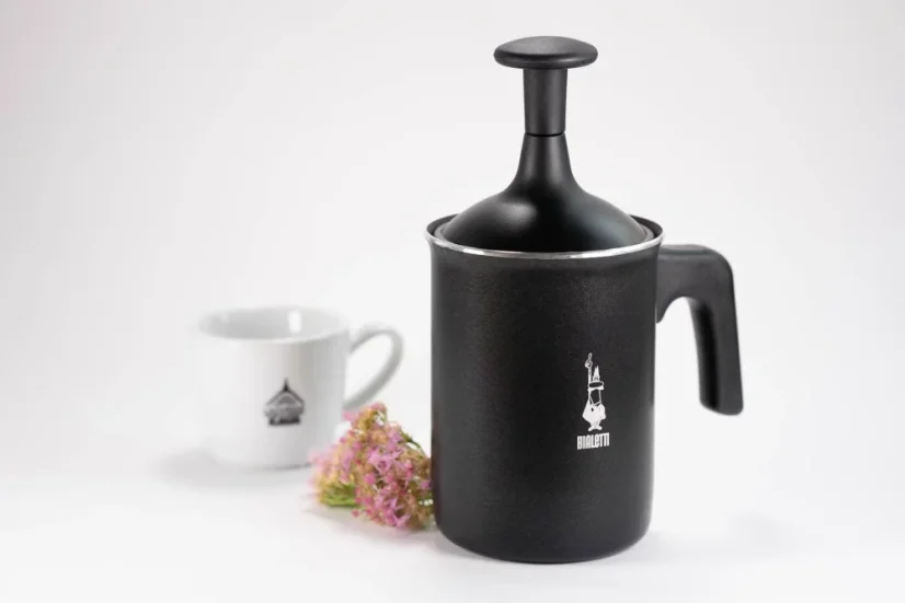 Milchaufschäumer in schwarzer Ausführung von Bialetti Tuttocrema mit einem Volumen von 330ml auf weißem Hintergrund zusammen mit einer Tasse und einem Wiesenblumenmotiv.