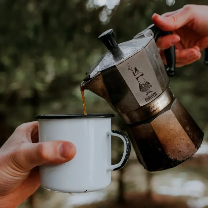 Pouring coffee prepared in a Bialetti Moka Express pot into a metal cup.