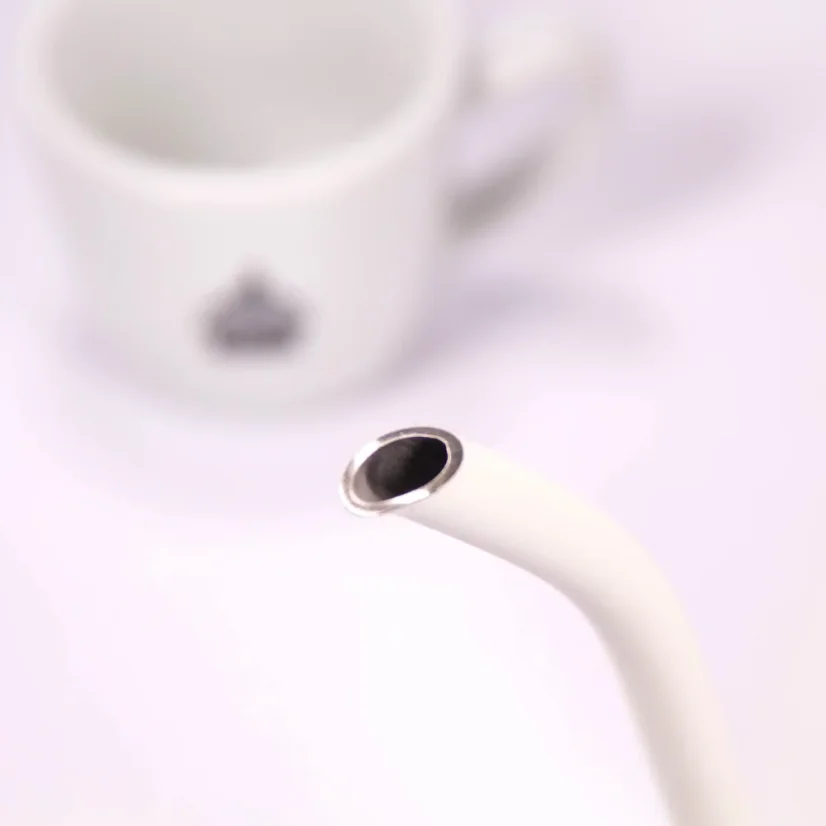Biela elektrická kanvica, detail na hrdlo kanvice, v pozadí šálka kávy