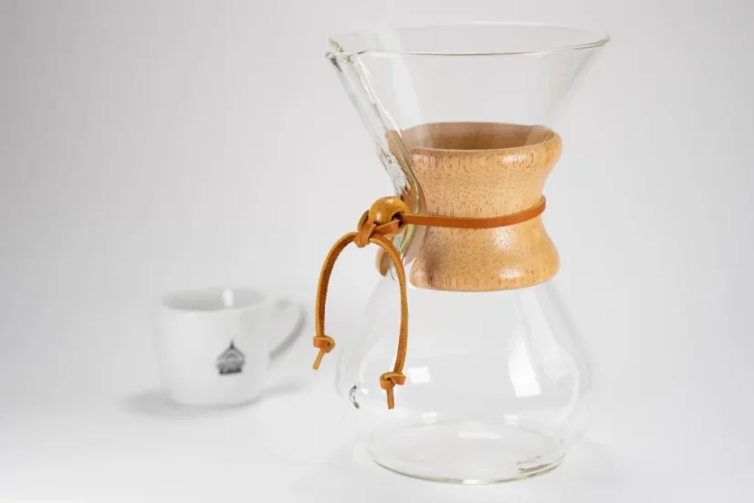 Chemex en verre avec une poignée en bois et une corde en cuir, tasse blanche à café avec logo sur fond blanc.