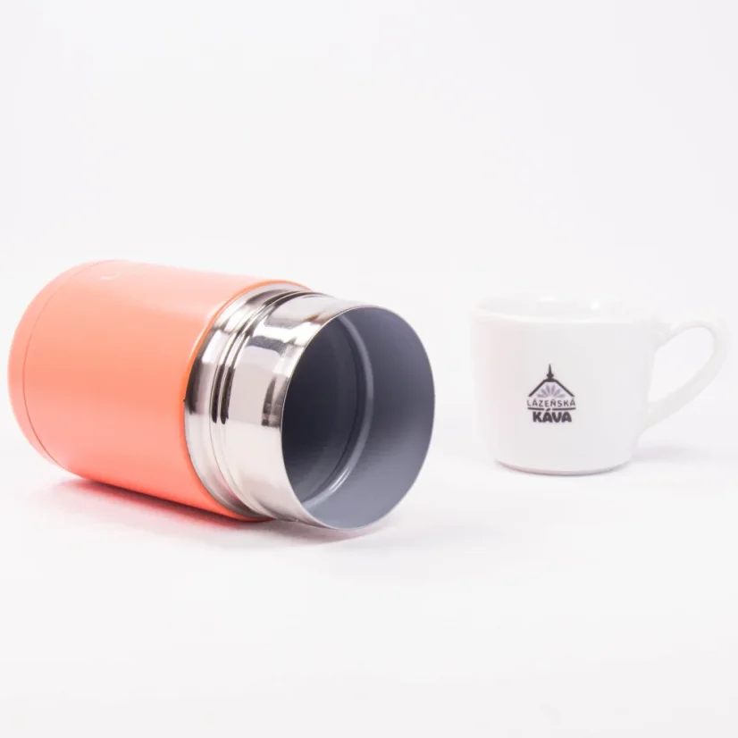Detail of an open coral thermal bottle lying on a white background with a cup of spa coffee