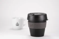 Plastinis juodas termosas su pilka rankena 227 ml tūrio, su puodeliu kavos ant baltos foninės dalies.