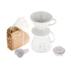 Zestaw Hario V60-02 Ceramic Driper w białym wykończeniu z ceramicznym dripperem, szklanym dzbankiem, plastową pokrywką, dozownikiem i brązowymi papierowymi filtrami.