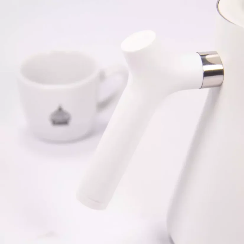 White electric kettle, detail on the kettle handle, with a cup of coffee in the background.
