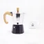 Moka pot with a black water funnel and wooden handle for 2 cups of coffee by Forever Miss Woody with a porcelain cup in the background