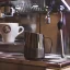 Nierdzewny dzbanek do spieniania mleka Barista a Co Dial in Milk Pitcher o pojemności 420 ml w ciemnym wykończeniu, na ekspresie do kawy z dyszą do spieniania mleka i filiżanką.