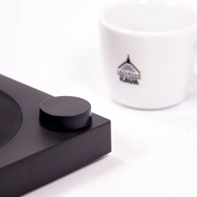 Detail of a black base of an electric kettle on a white background with a cup of coffee
