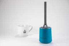 Escorredor de plástico cinza com recipiente azul para apoio e, ao fundo, uma xícara de porcelana com logotipo.