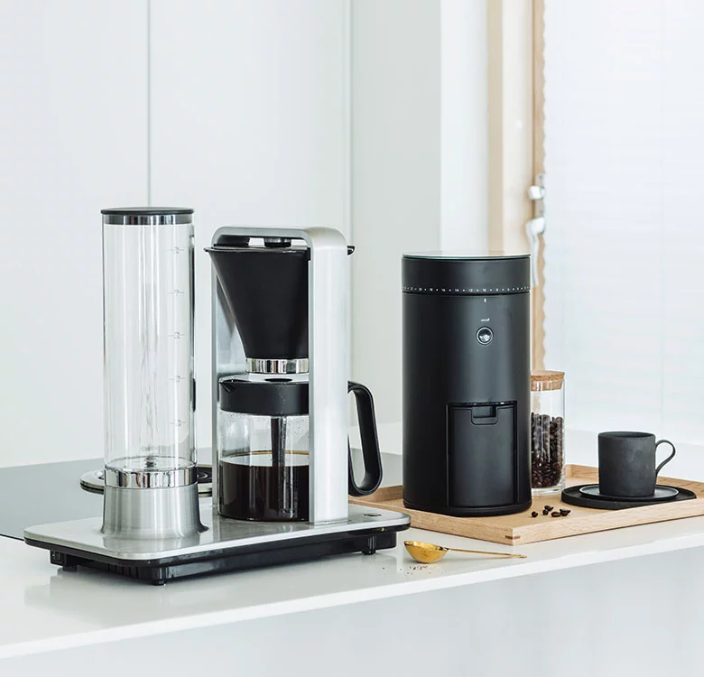 Side view of a Wilfa drip coffee maker with an electric coffee grinder on a kitchen countertop.