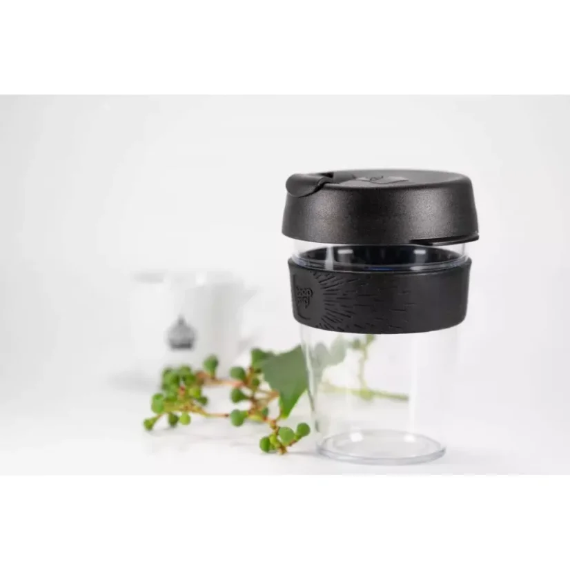 Gobelet thermique en plastique avec un support en caoutchouc sur une table blanche avec des plantes et un gobelet blanc avec logo.