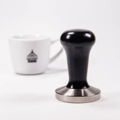 Tamper 58,4 mm s čiernou rukoväťou a šálka na kávu.