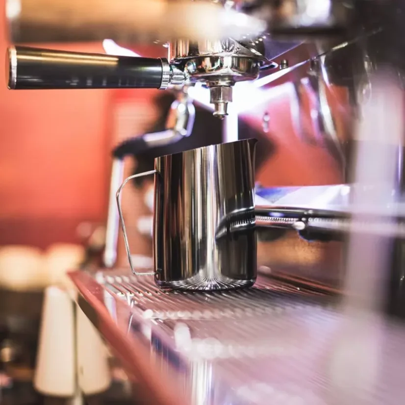 Cruche noire pour mousser le lait de Barista a Co Dial d'une capacité de 60 ml posée sur un café avec un arrière-plan coloré.