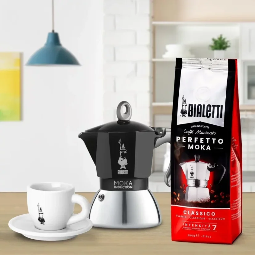 Kávéfőző Bialetti New Moka Induction egy fehér csészével és egy kávécsomaggal, az olasz Bialetti márkájú logóval.