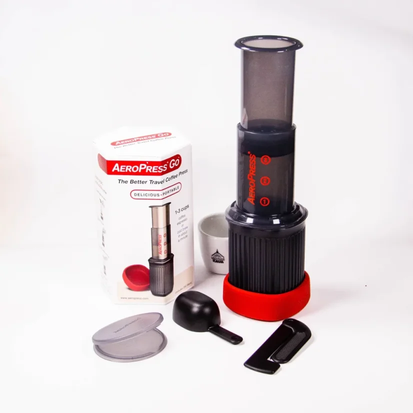 AeroPress Go disassembled into components next to the original packaging on a white background