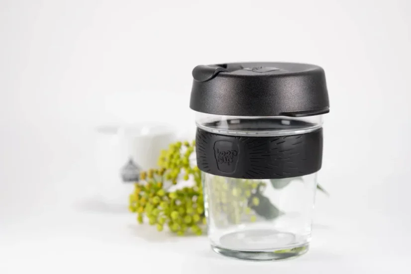 Gobelet thermique en verre avec couvercle noir et support en caoutchouc noir d'une capacité de 340 ml, décoré d'une petite branche et d'une tasse de café.