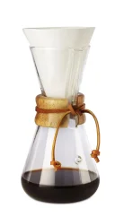 Glass Chemex with an elongated head, wooden handle, and leather string, white paper filter, coffee prepared in the Chemex.