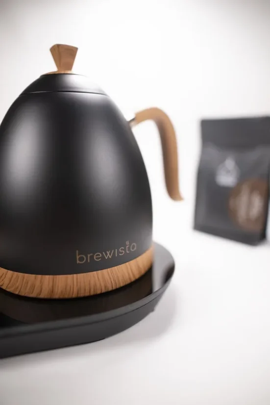 Elegantná rýchlovarná kanvica značky Brewista na podstavci v matne čiernej úprave s elegantným úchopom a možnosťou regulácie teploty v pozadí s našou praženou kávou.