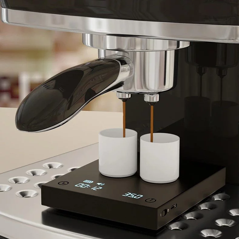 Digital scale Black Mirror used in espresso preparation with two white cups and a portafilter.